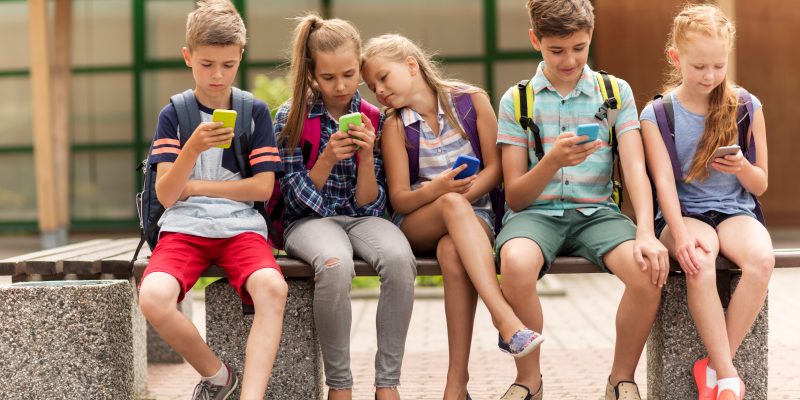 Mehrere Kinder auf Parkbank mit ihren Smartphones in der Hand